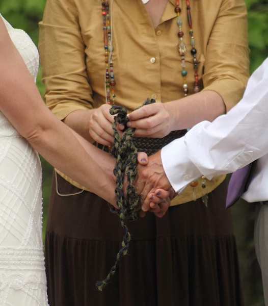 Wedding officiant ties hand-fasting cord as bride and groom hold hands